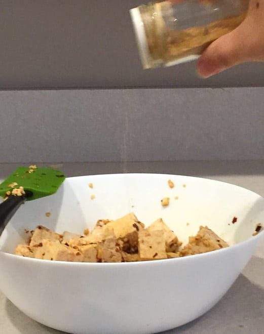 A bowl of tofu with ingredients being added in for marination.