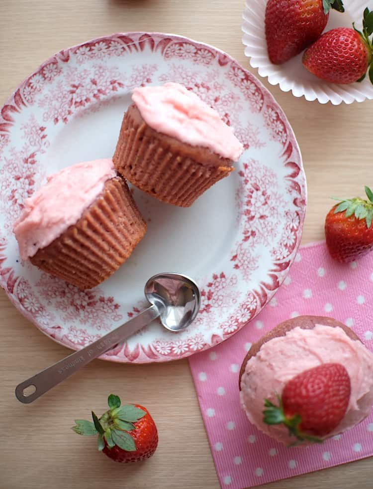 Strawberry cupcake flat lay with vegan strawberry cupcakes frosted with pink strawberry icing, and lots of fresh strawberries scattered about.