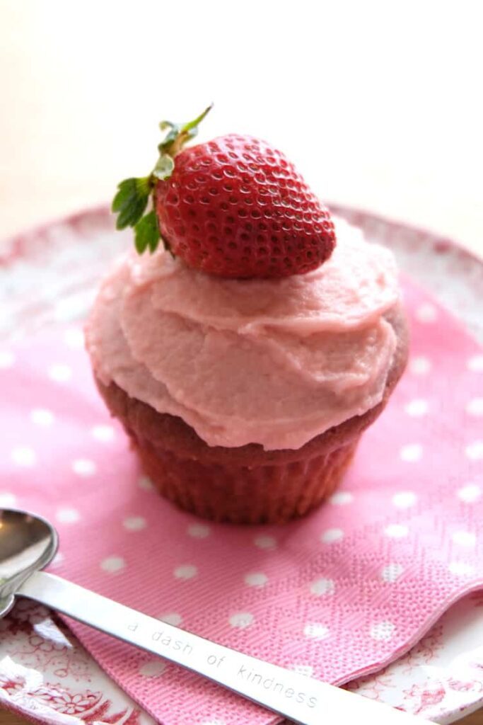 a strawberry cupcake with strawberry icing and a fresh strawberry on top