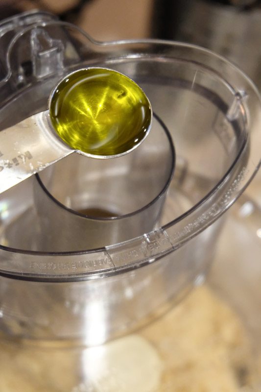 Adding the olive oil one tablespoon at a time to the sesame seeds.