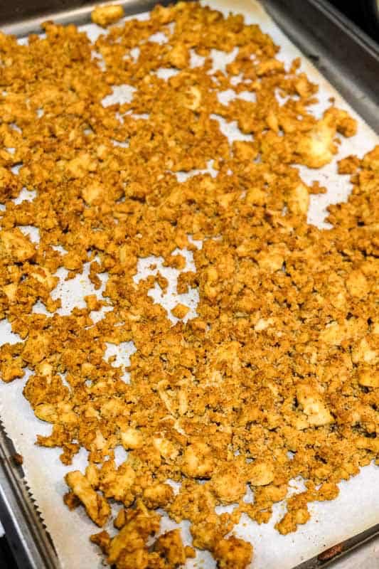 Crumbled tofu on a baking sheet lined with parchment, slightly browned after cooking.