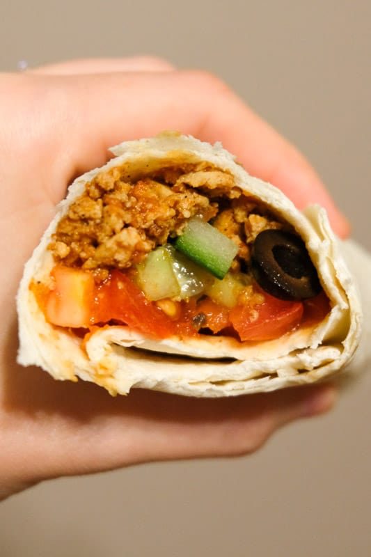 Cutaway view of a burrito with sofritas instead of beef taco meat inside, it also contains cucumbers, tomatoes, salsa, and black olives.