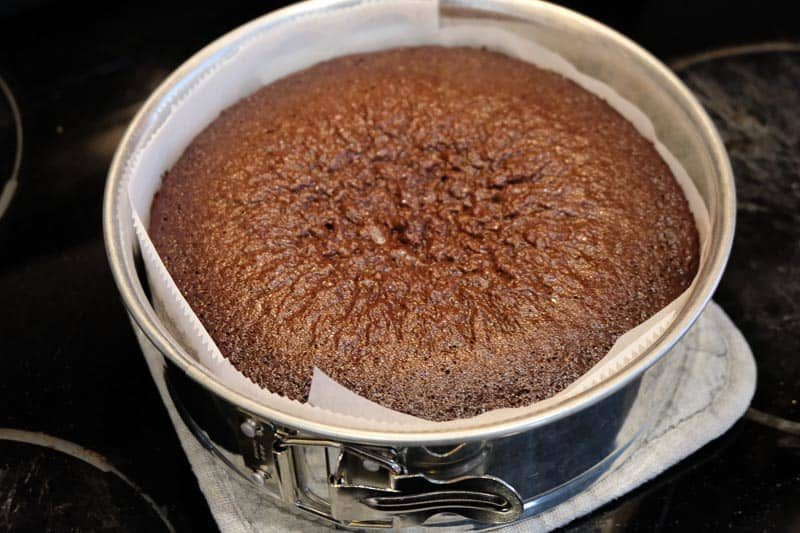 A cooked chocolate cake cooling on the stove, still in the springform pan lined with parchment paper.