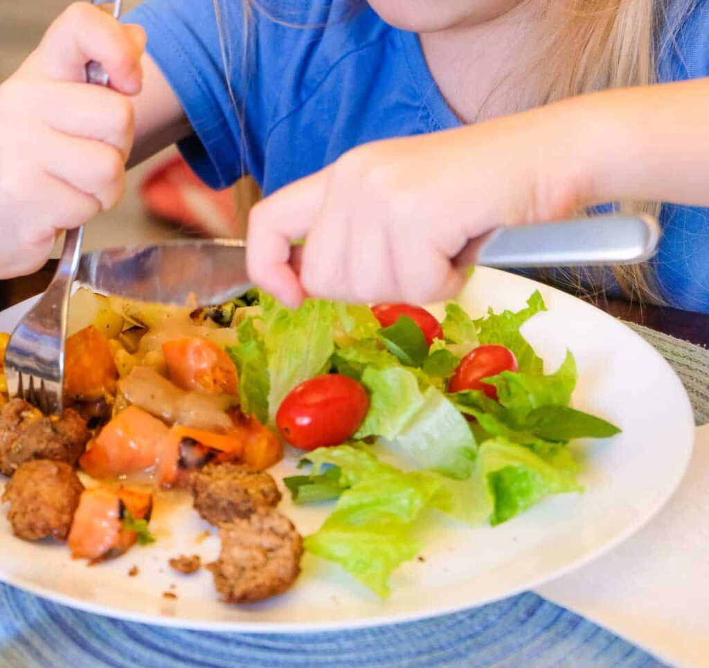 Child eating a vegan dinner of roasted veggies, vegan gravy, and a side salad.