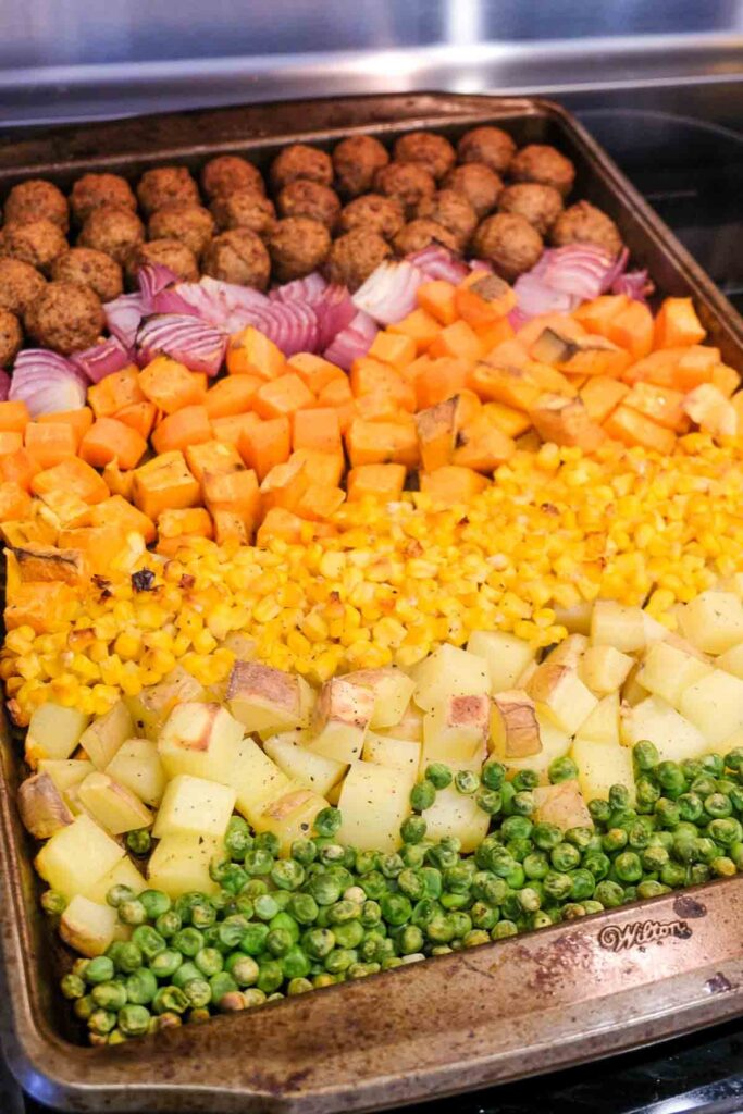 A sheet pan with roasted vegetables and plant-based meatballs arranged in rainbow stripes.