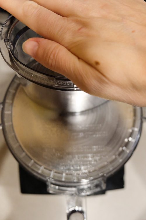 A hand pushing a potato into a food processor.