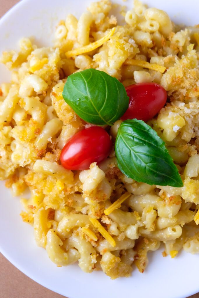 Baked vegan mac and cheese on a plate, it has a breadcrumb crust and is garnished with cherry tomato and basil leaves.