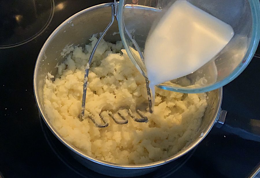Oat milk being poured into a pot of mashed potatoes on the stove.