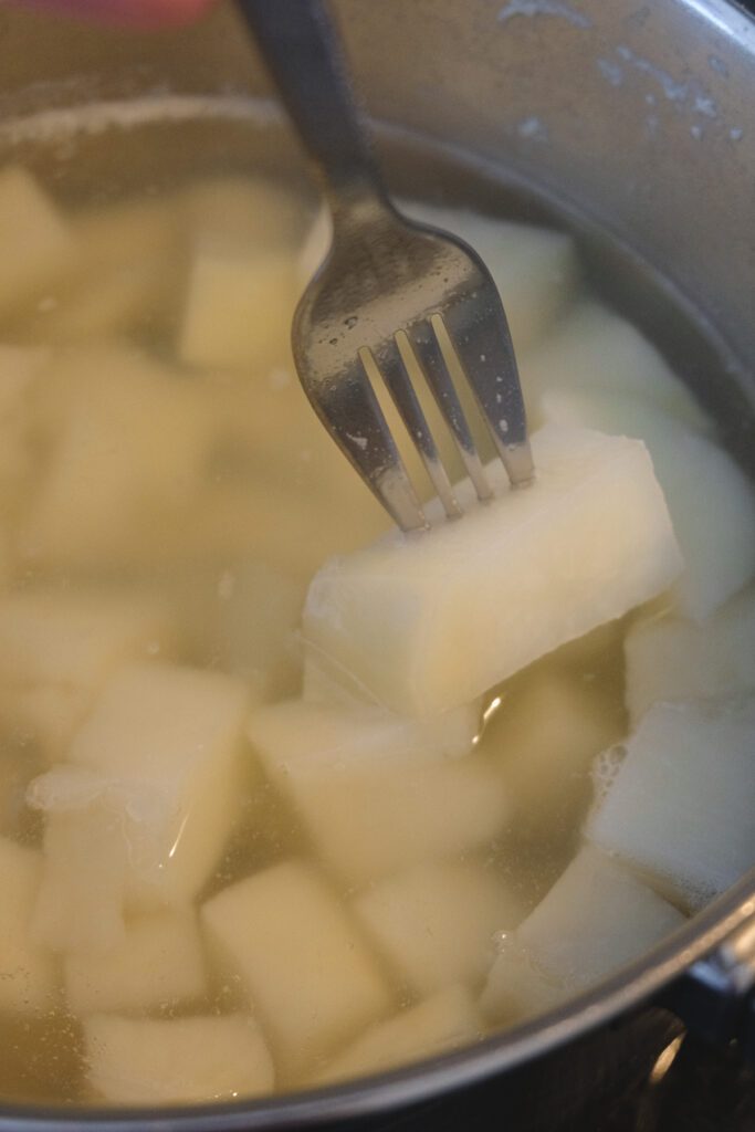 Close-up view of a fork sticking into a potato piece in a pot of boiling-hot water.
