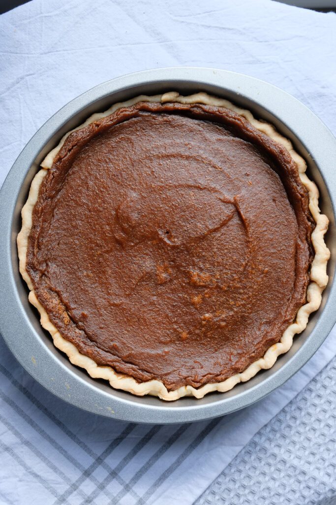 A vegan pumpkin pie cooling off in the pie plate on a table covered with kitchen towels.