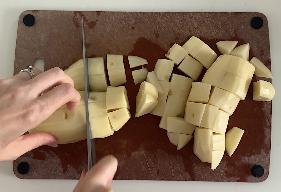 Top-down view of a person cutting potatoes into 1" cubes.