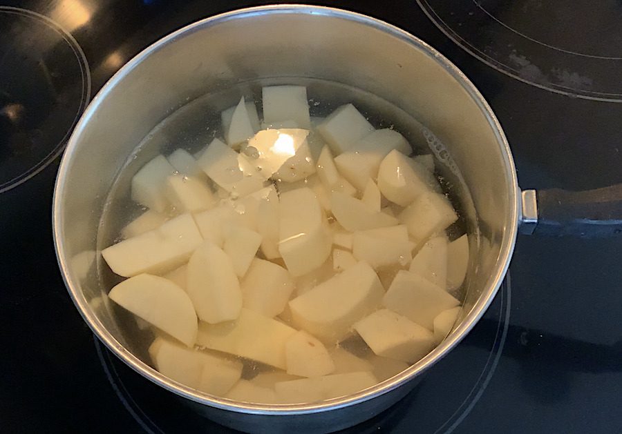 Cut potato pieces in a pot with some water on a stove.
