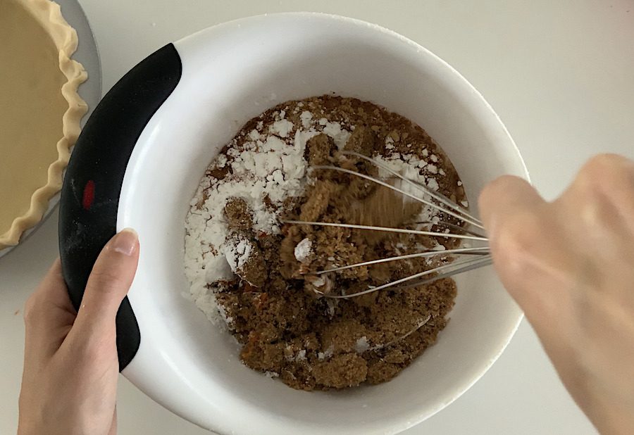 A bowl of pumpkin pie ingredients such as brown sugar, cooked pumpkin from a can, corn starch, and coconut milk, being whisked together.