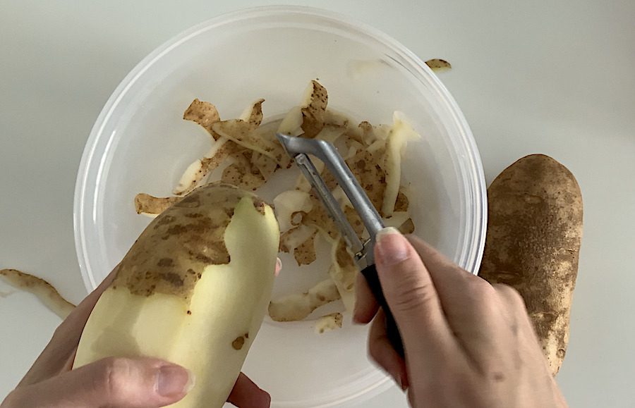 Top-down view of a person's hands peeling russet potatoes.